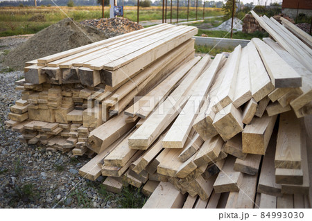 Close-up of piled stack of natural brown uneven rough wooden boards lit by bright sun. Industrial timber for carpentry, building, repairing and furniture, lumber material for construction. Close-up of piled stack of natural brown uneven rough wooden boards lit by bright sun. Industrial timber for carpentry, building, repairing and furniture, lumber material for construction. 84993030
