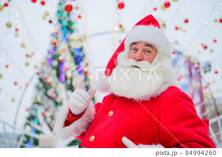 Portrait of an elderly man dressed as santa claus on the background of a christmas tree outdoors. Portrait of an elderly man dressed as santa claus on the background of a christmas tree outdoors. 84994260