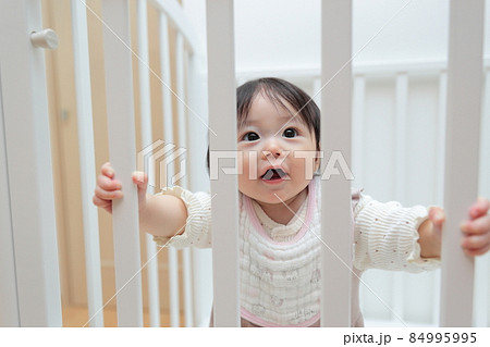 つかまり立ちをする生後半年の赤ちゃんの女の子の写真素材