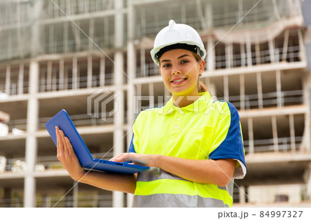 Young woman engineer holds a laptop in her hands, watching the construction process 84997327