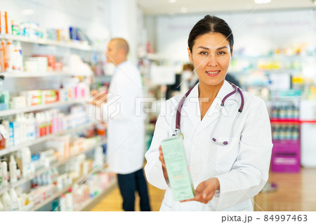 Female pharmacist offers medicine while standing in the trading floor of pharmacy Female pharmacist offers medicine while standing in the trading floor of pharmacy 84997463