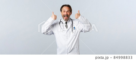 Covid-19, coronavirus outbreak, healthcare workers and pandemic concept. Excited upbeat male doctor in white coat thumbs-up in approval. Surgeon agree or like idea, recommend promo 84998833