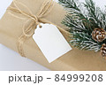 Christmas and New Years background close-up. Gift box wrapped in kraft paper with jute cord. Decorated with a label and a branch with cones 84999208