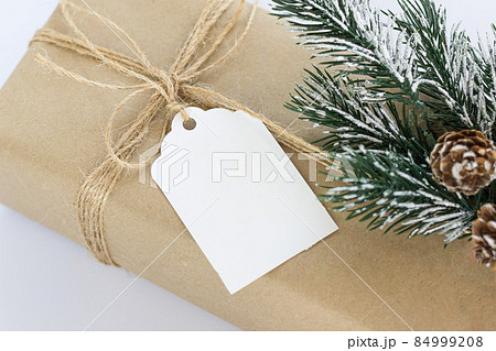 Christmas and New Years background close-up. Gift box wrapped in kraft paper with jute cord. Decorated with a label and a branch with cones 84999208