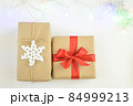 Christmas and New Year background with garland. Gift box wrapped in kraft paper with jute cord. Decorated with a crocheted snowflake. Box with a red ribbon 84999213