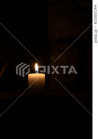 A candle burns against the background of masonry in the dark. Front view. A candle burns against the background of masonry in the dark. Front view. 85000144