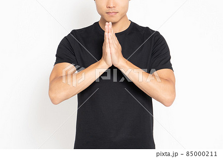 白い背景の前に立って手を合わせる黒いTシャツを着ている男性 85000211
