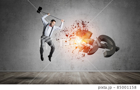 Determined banker man in empty concrete room breaking dollar figure Determined banker man in empty concrete room breaking dollar figure 85001158