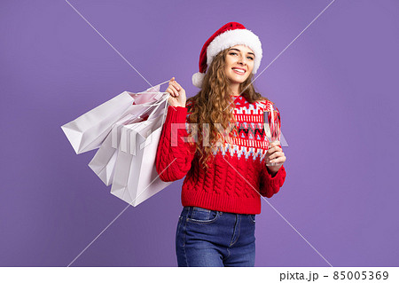 Santa girl holds shopping bags and champagne on purple background. Christmas sales. Black Friday Santa girl holds shopping bags and champagne on purple background. Christmas sales. Black Friday 85005369
