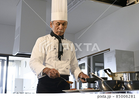 飲食店の厨房でコック服を着たシニア男性が料理を作る 85006281