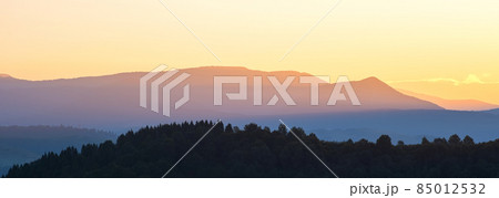 Beautiful mountain panorama of landscape with hazy peaks and foggy wooded valley at sunset. 85012532