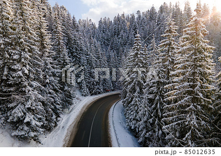Aerial view of winter landscape with snow covered mountain hills and winding forest road in morning. Aerial view of winter landscape with snow covered mountain hills and winding forest road in morning. 85012635