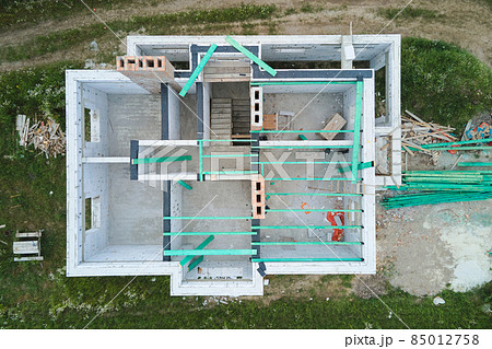 Aerial view of unfinished frame of private house with aerated lightweight concrete walls and wooden roof beams under construction. Aerial view of unfinished frame of private house with aerated lightweight concrete walls and wooden roof beams under construction. 85012758