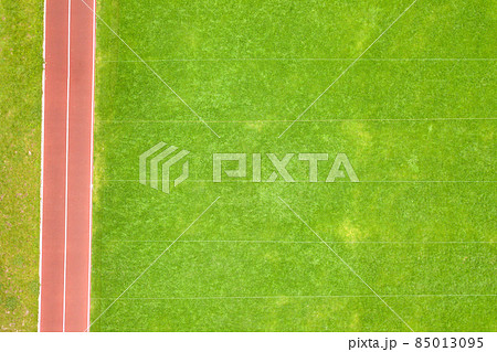 Aerial view of surface of green freshly cut grass on football stadium field with red running tracks in summer. 85013095