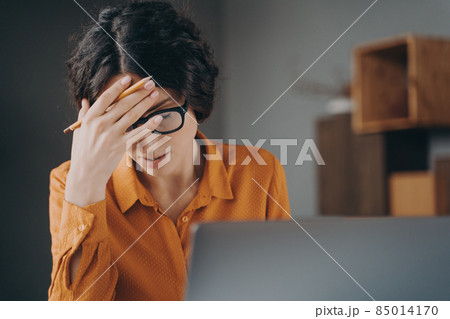 Frustrated tired young Spanish woman office worker in glasses covering face with hand 85014170
