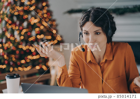 Callcenter female consultant in headset talking with customer while working during Christmas holidays Callcenter female consultant in headset talking with customer while working during Christmas holidays 85014171