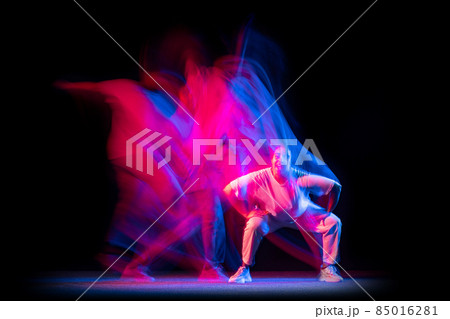 Sportive young girl in white costume dancing hip-hop dance isolated on dark background at dance hall in neon mixed light. 85016281