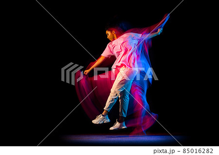 Stylish young girl in white costume dancing hip-hop dance isolated on dark background at dance hall in neon mixed light. Stylish young girl in white costume dancing hip-hop dance isolated on dark background at dance hall in neon mixed light. 85016282