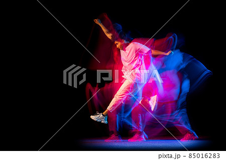 Excited young girl in white costume dancing hip-hop dance isolated on dark background at dance hall in neon mixed light. 85016283