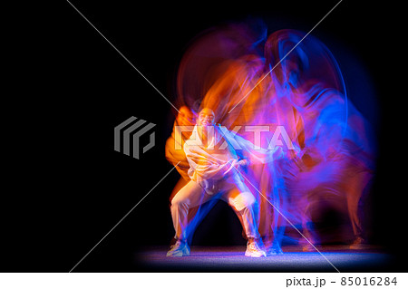 Stylish young girl in white costume dancing hip-hop dance isolated on dark background at dance hall in neon mixed light. 85016284