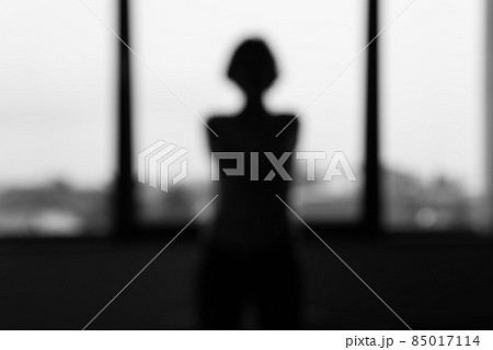 Young white woman standing in front of a window, facing her back. 85017114