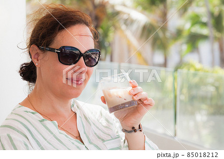 Young smiling woman in sunglasses drinking a cocktail with ice 85018212
