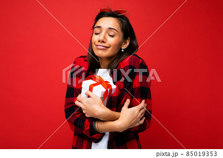 Pretty positive cute young brunette woman isolated over red background wall wearing white casual t Pretty positive cute young brunette woman isolated over red background wall wearing white casual t 85019353