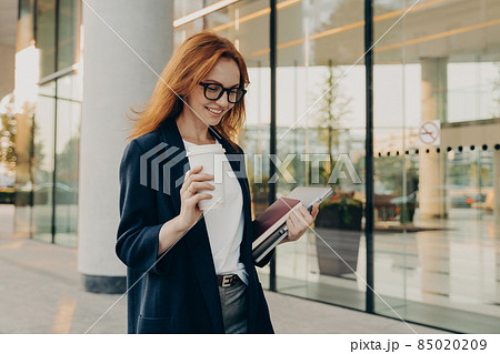 Smiling redhead woman corporate worker dressed in formal clothes drinks coffee 85020209