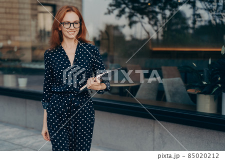 Cheerful prosperous businesswoman in elegant outfit holds tablet and diar 85020212