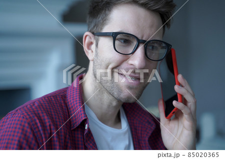 Young smiling german guy in glasses using mobile phone and talking on with friend Young smiling german guy in glasses using mobile phone and talking on with friend 85020365