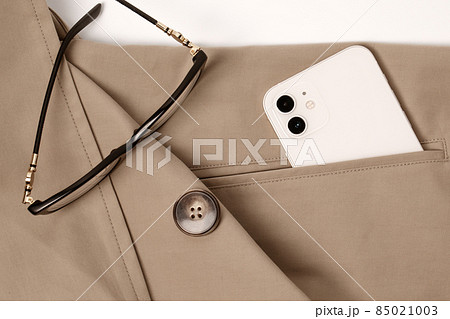Modern smart phone in cream colour and glasses in the pocket of beige trench coat Modern smart phone in cream colour and glasses in the pocket of beige trench coat 85021003
