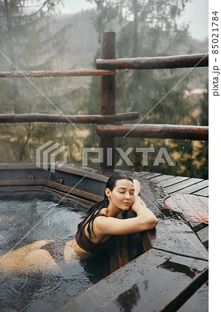 Woman in bikini bathing in Japanese style bath outdoors 85021784