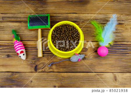 Dry cat food in bowl, cat toys and pet slicker brush on wooden background. Top view. Pet care concept 85021938