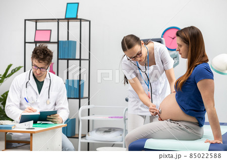 Your doctor auscultates a pregnant patient's abdomen with a stethoscope. The attending physician completes the appointment calendar. Your doctor auscultates a pregnant patient's abdomen with a stethoscope. The attending physician completes the appointment calendar. 85022588