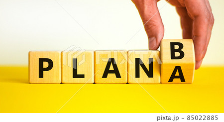 Plan A or B symbol. Businessman turns a wooden cube and changes words Plan A to Plan B. Beautiful yellow table, white background, copy space. Business and Plan A or B planning concept. 85022885