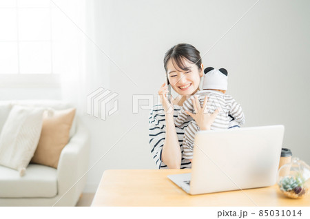 赤ちゃんを抱きながらパソコンを使う女性 85031014