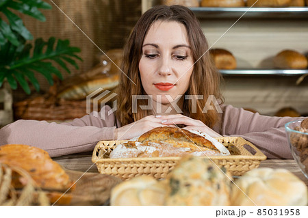 During a break, an attractive saleswoman looks at her freshly baked bread, especially one loaf of bread, which with its cracked crust distinguishes it from others. Family bakery shop with multi 85031958