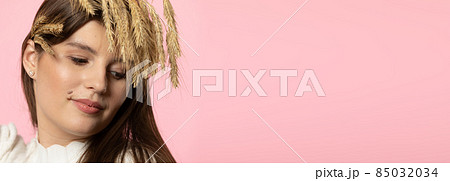 Panoramic frame. Portrait of an attractive young girl with colossi of grain in her hair. The whole is isolated from a uniform light pink background. Panoramic frame. Portrait of an attractive young girl with colossi of grain in her hair. The whole is isolated from a uniform light pink background. 85032034