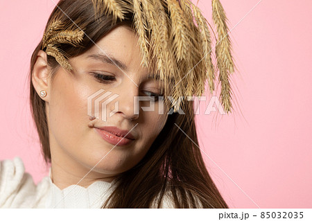 Portrait of an attractive young girl with colossi of grain in her hair. The whole is isolated from a uniform light pink background. Portrait of an attractive young girl with colossi of grain in her hair. The whole is isolated from a uniform light pink background. 85032035