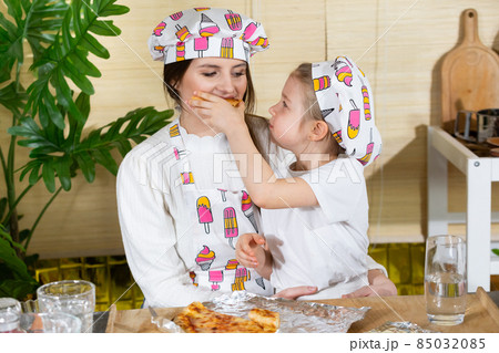 A five-year-old daughter feeds her mom with a freshly baked homemade pizza. Together and unforgettable moments, mothers and daughters in the home kitchen. 85032085