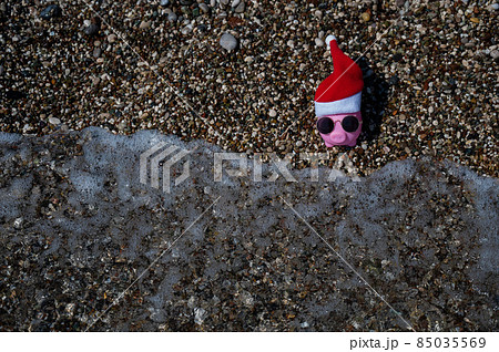 Piggy bank in a hat of santa claus and sunglasses on a pebble beach by the sea. Piggy bank in a hat of santa claus and sunglasses on a pebble beach by the sea. 85035569