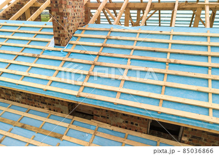 Aerial view of a brick house with wooden roof frame under construction. 85036866