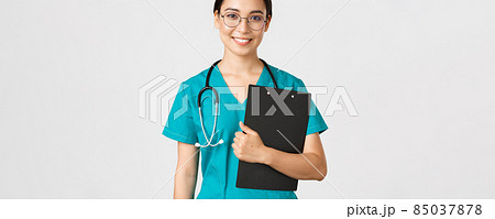 Covid-19, coronavirus disease, healthcare workers concept. Smiling confident asian female nurse, physician in glasses and scrubs holding clipboard, making examination, white background Covid-19, coronavirus disease, healthcare workers concept. Smiling confident asian female nurse, physician in glasses and scrubs holding clipboard, making examination, white background 85037878
