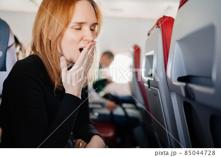 a sleepy woman yawns in an airplane seat. long flights. a sleepy woman yawns in an airplane seat. long flights. 85044728