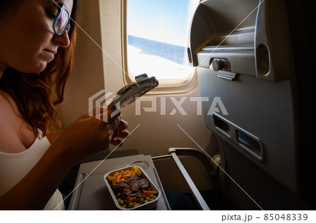 Caucasian woman flying in economy class and eating lunch from a tray table on board the plane. 85048339