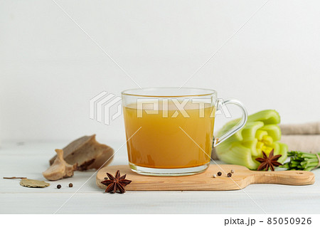 Meat broth with spices and vegetables in a mug, on a wooden board. Close-up. On a gray background, horizontal 85050926