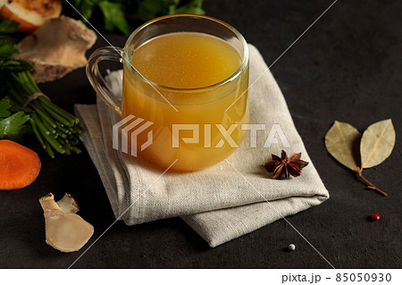 Homemade beef broth with vegetables in a glass mug. Close-up on a black background 85050930