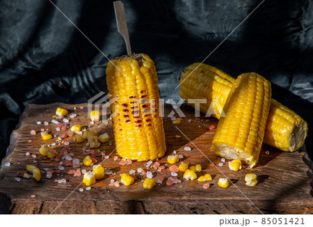 Grilled corn on the cob on rustic wooden board over dark background. Grilled corn on the cob on rustic wooden board over dark background. 85051421