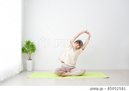 屋内でマットを敷いてストレッチする若い女性 85052581