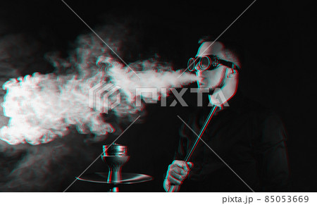 man in futuristic glasses smokes a hookah and blows a cloud of smoke in a shisha bar 85053669